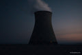 Silhouetted industrial cooling tower at dusk with steam rising against twilight sky